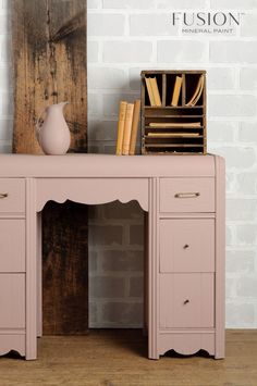 a pink desk with some books on it and a vase sitting on top of it