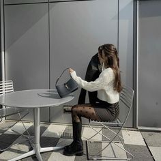 a woman sitting at a table with a purse in her hand and wearing black tights