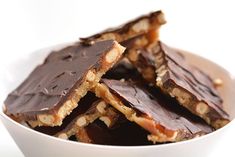 a white bowl filled with pieces of chocolate and nuts on top of each other in front of a white background