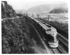 a black and white photo of a train going down the tracks near a rocky mountain