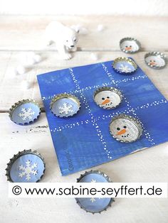 snowman bottle cap magnets sitting on top of a blue board with white snowflakes