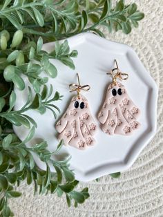 two pink earrings with googly eyes are on a white plate next to green leaves