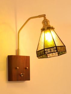 a wall light with a wooden frame and green glass shade hanging from it's side