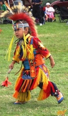 a young child dressed in native american clothing and headdress, walking through the grass