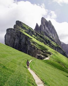 a man walking down a path in the mountains with grass and rocks on either side