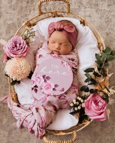 a newborn baby is sleeping in a wicker basket with flowers and a sign that says i'm here