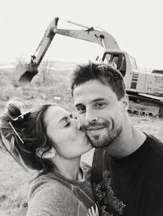 a man and woman kissing each other in front of a construction site with an excavator behind them