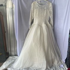 a white wedding dress is hanging on a clothes rack in front of a curtain and some other items