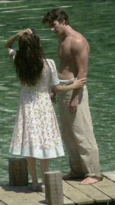 a man standing next to a woman on top of a wooden pier near the water