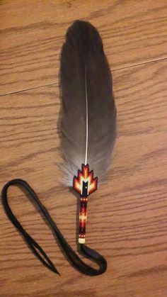 a feather is laying on the floor next to a black leather strap and an orange, white, and red bead