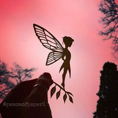 a person holding up a paper cut out of a fairy with leaves on it's tail