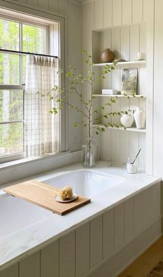 a white bath tub sitting under a window next to a shelf filled with vases