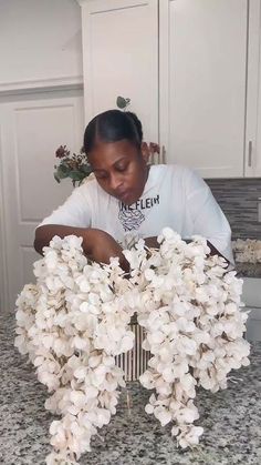 a woman arranging white flowers on top of a kitchen counter