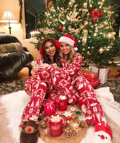 two women in matching christmas pajamas sitting on a coffee table next to a christmas tree