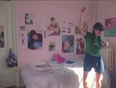 a young boy standing on top of a bed in a room with pink walls and posters