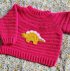 a pink sweater with a yellow dinosaur applique is laying on a floral surface