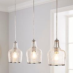 three clear glass pendant lights hanging from a ceiling fixture in a room with white walls