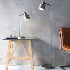 a table with a lamp on it next to a brown chair and a gray wall