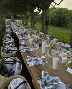 a long table is set with place settings and candles for an outdoor dinner in the garden