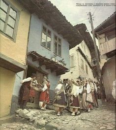 an old photo of people standing in front of a blue and yellow building on cobblestone street