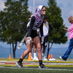 a woman in black and white running on a field with other people watching from the sidelines