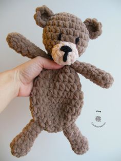 a crocheted teddy bear being held up by someone's hand, against a white background