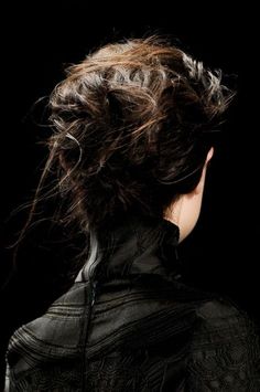 the back of a woman's head with her hair blowing in the wind, against a black background