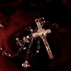 a cross and rosary on a red rose in the dark with light shining through it