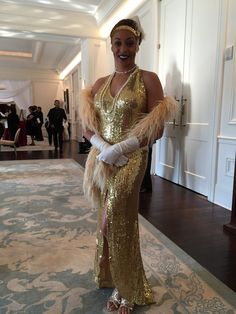 a woman in a gold dress and white gloves standing next to a carpeted hallway