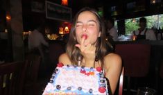 a woman sitting at a table in front of a cake with candles on it and her tongue sticking out