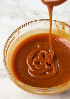 sauce being poured into a bowl with a spoon in it on a marble countertop