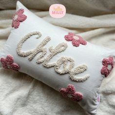 a white pillow with pink flowers and the word love written on it in cursive letters