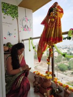 a woman sitting in front of a window looking at flowers and decorations on the ground