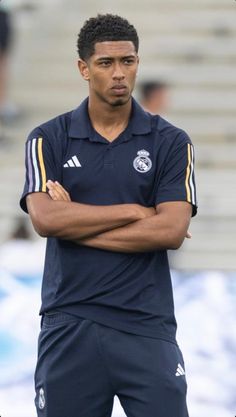 a man standing with his arms crossed in front of him on a soccer field wearing a blue shirt and shorts