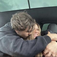 a man and woman sitting in the back seat of a car, hugging each other