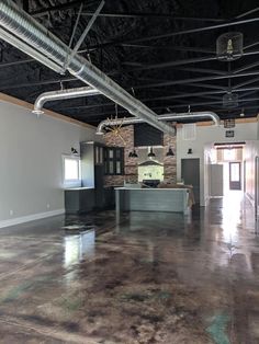 an empty kitchen and living room in a building with exposed ceilings, concrete flooring and metal pipes