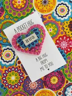 a greeting card with a heart shaped brooch on top of a colorful floral background