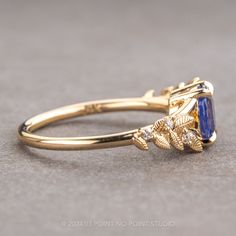 a yellow gold ring with an oval blue stone surrounded by small white diamonds and leaves