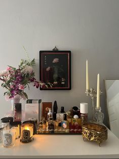 a white table topped with lots of bottles and candles next to a vase filled with flowers