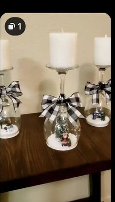 three clear glass vases with christmas decorations in them on a wooden table next to two white candles