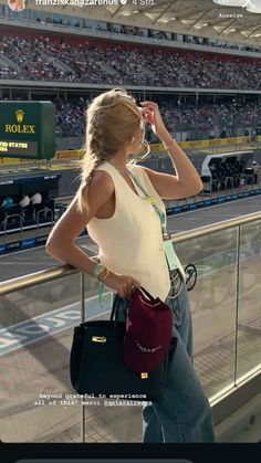 a woman standing in front of a stadium holding a purse and talking on her cell phone