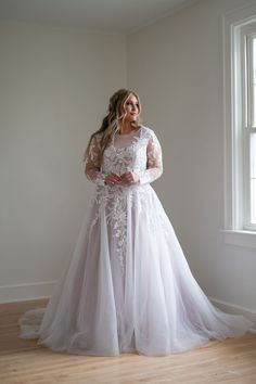 a woman in a white wedding dress standing on a wooden floor next to a window