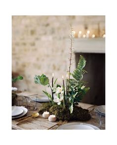 an arrangement of white flowers and greenery on a table in front of a brick wall