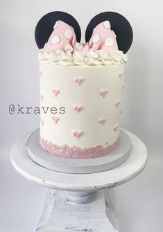 a minnie mouse cake with pink and white frosting on top is sitting on a pedestal