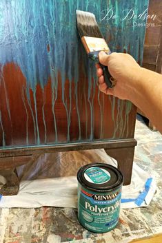 a person is holding a paintbrush and painting an old dresser