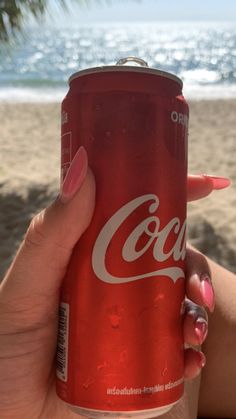 a woman holding up a can of coca - cola on the beach