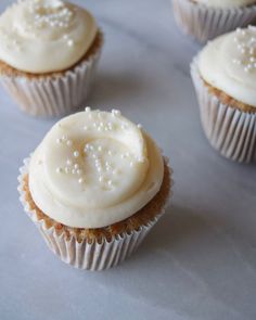 four cupcakes with white frosting and sprinkles on the top