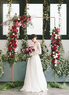 a woman in a wedding dress standing next to a wall with flowers and greenery