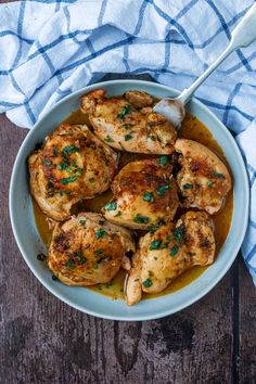 a bowl filled with chicken and sauce on top of a wooden table next to a blue towel