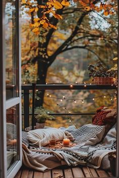 an open window with blankets and candles on the outside deck in front of some trees